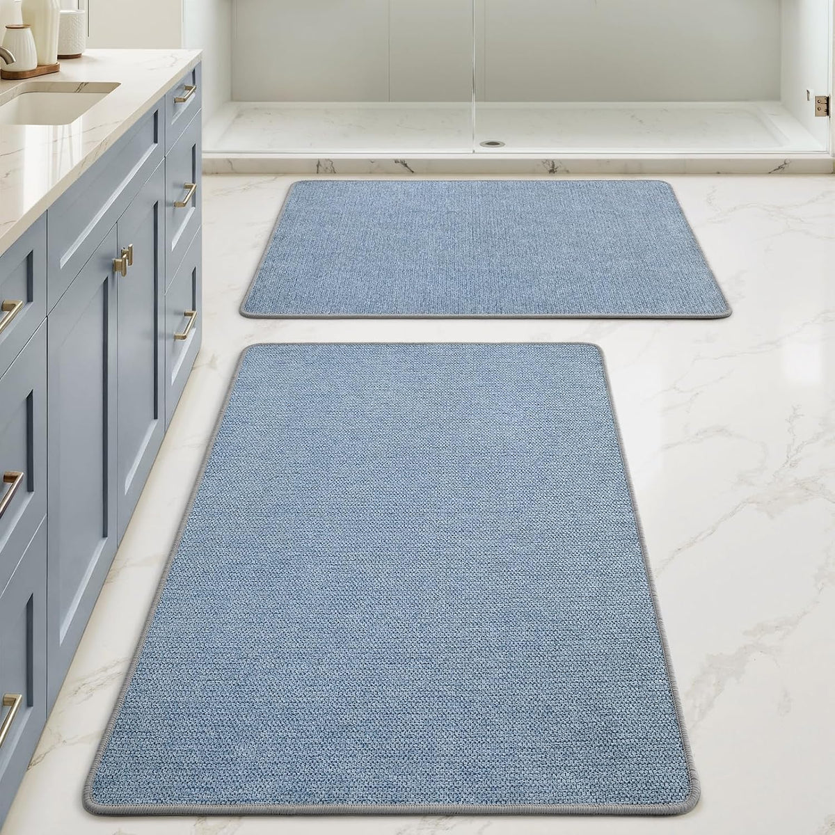 Two light-blue rectangular bath mats positioned down the center of a bathroom with blue-toned cabinets at left.