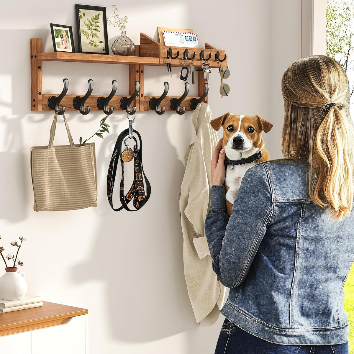 Wall-mounted wooden coat rack with shelf showing 11 black metal hooks and a woman holding a small dog.
