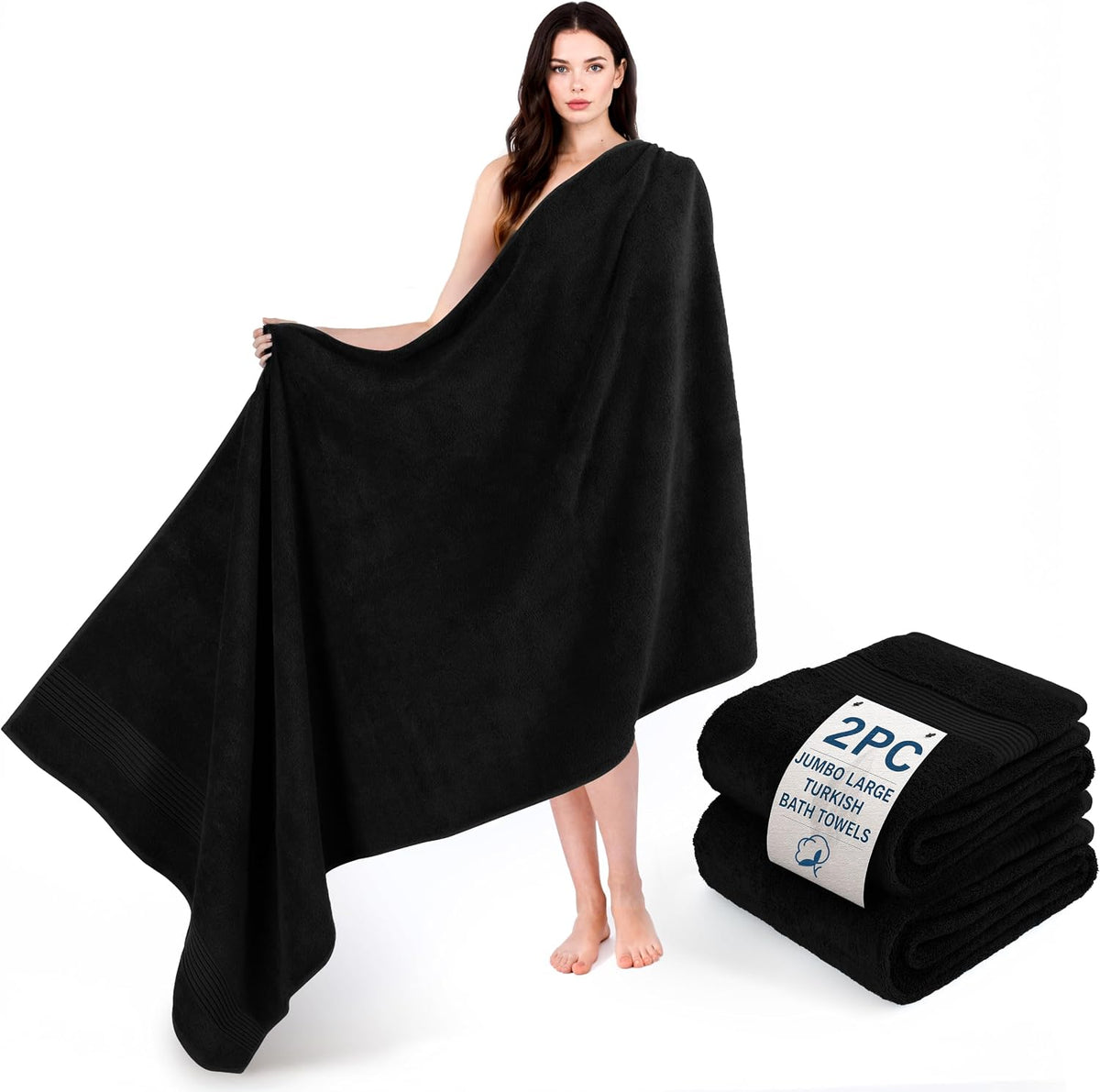 Woman draped in a large black towel standing next to two folded black towels on a white background.