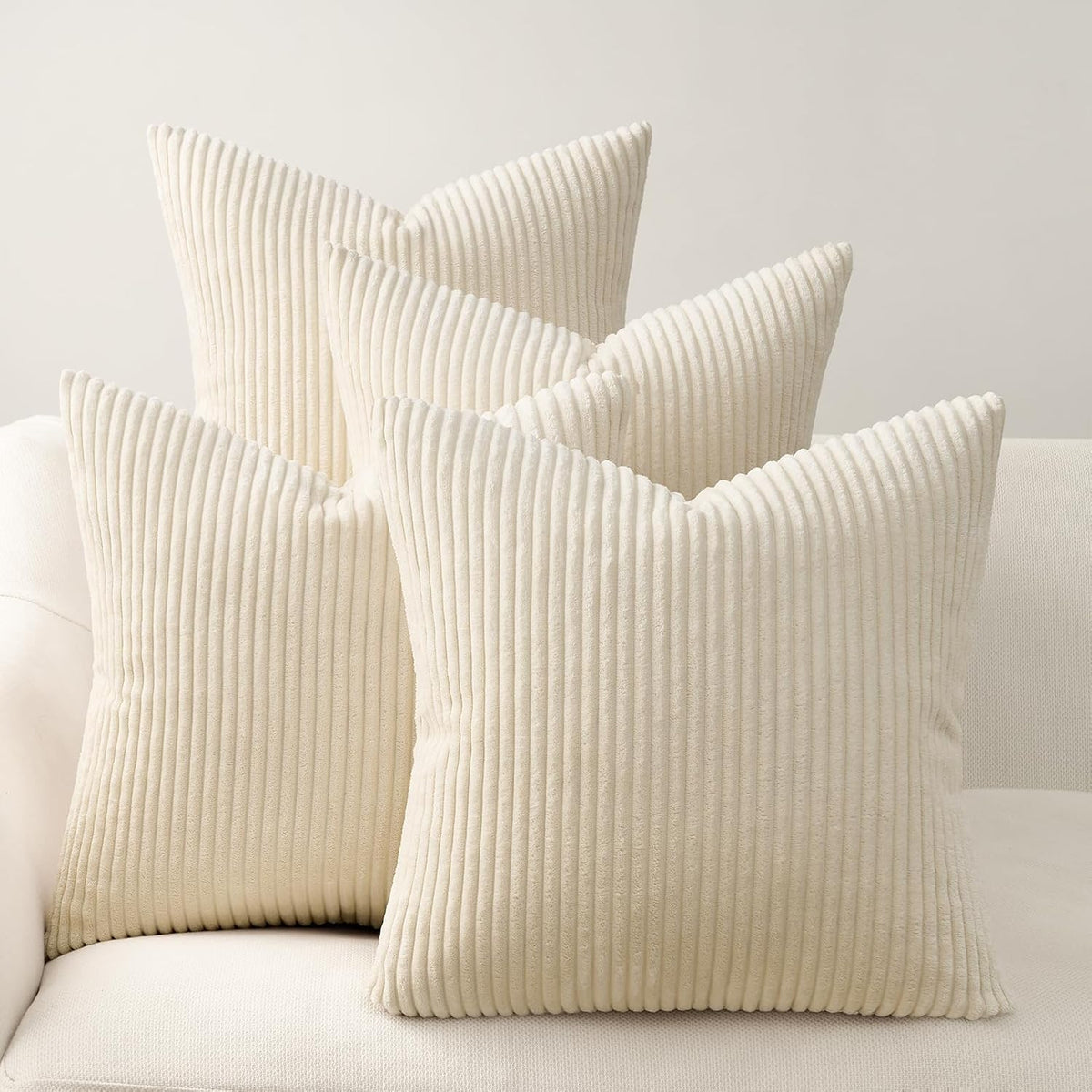 Four cream, ribbed corduroy square pillows arranged on a light sofa