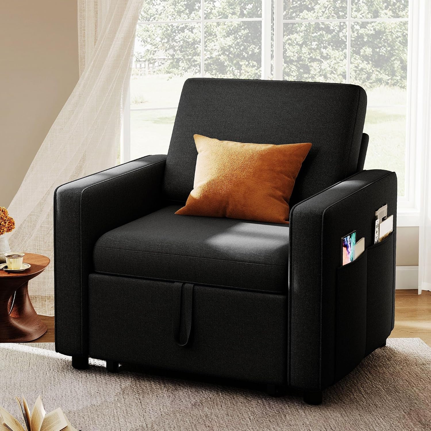 Black convertible chair in a bright room with an orange throw pillow and side storage pockets.