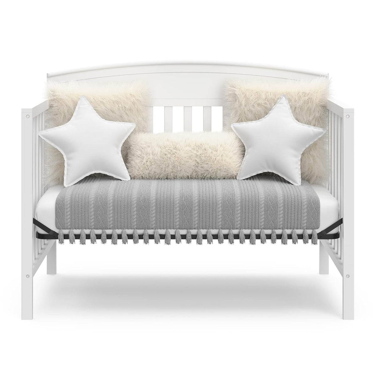 Front view of the crib converted to a daybed, styled with a gray throw, faux-fur bolsters and star-shaped pillows.
