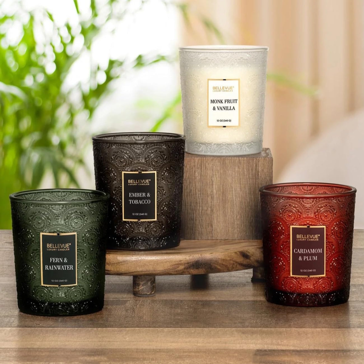 Styled display of four embossed glass jar candles on a wooden surface with greenery in the blurred background