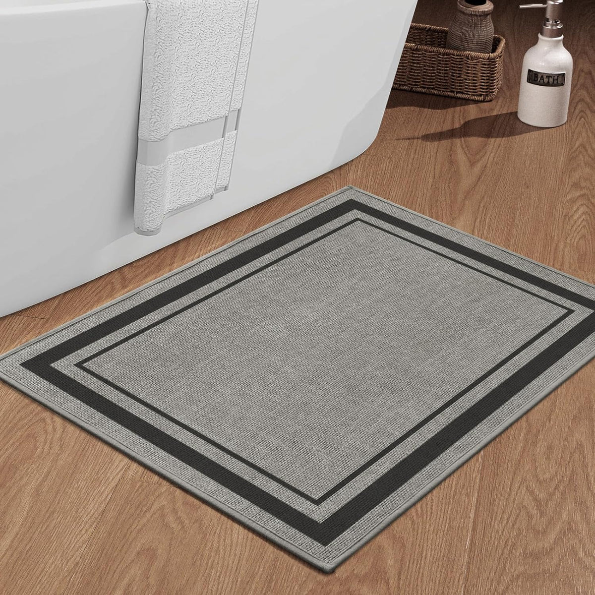 Close-up of a gray rectangular bath rug with twin inner and outer stripes placed at a bathtub side.