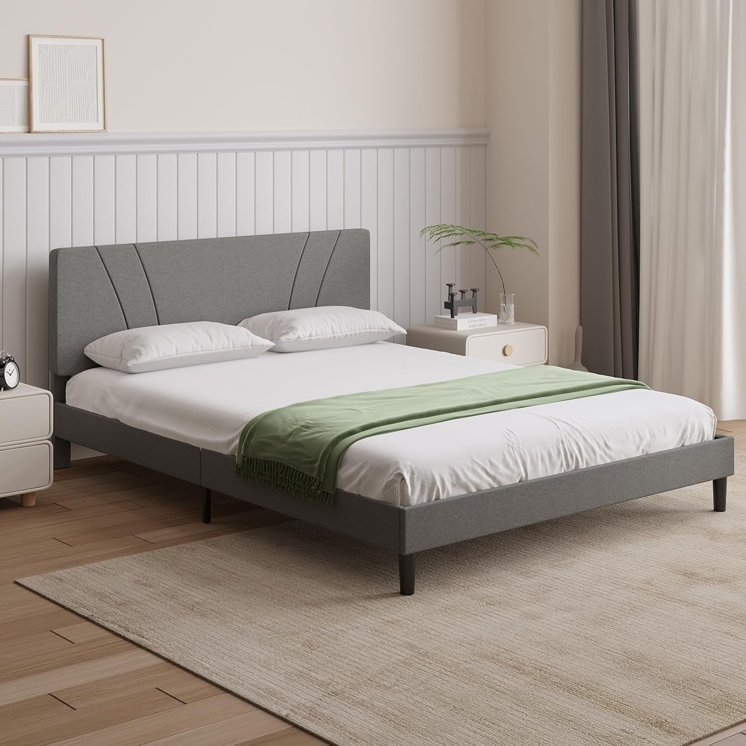Angled bedroom view of a gray upholstered platform bed with a fan-pattern headboard and green throw.