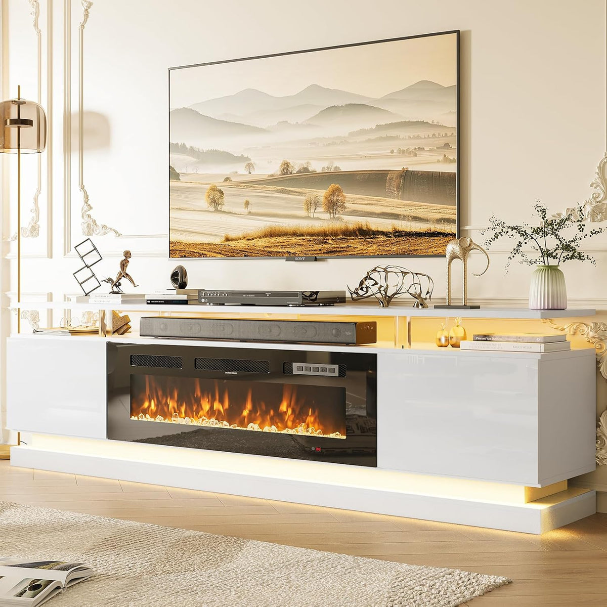 Front view of a white glossy TV stand with integrated electric fireplace and soft warm underlighting beneath a landscape TV.