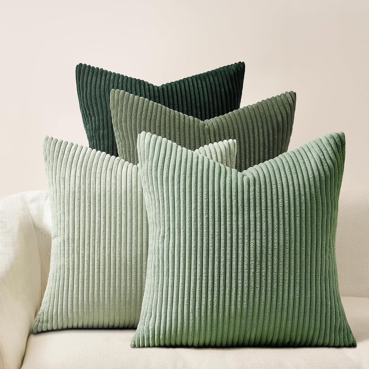 Five ribbed corduroy pillows in varying shades of green displayed on a pale couch