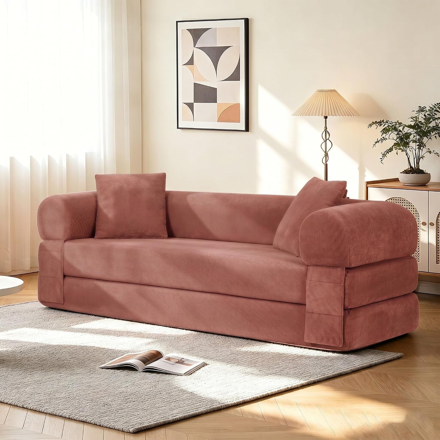 Angled view of a dusty rose corduroy sofa with two pillows on a rug near a lamp and cabinet