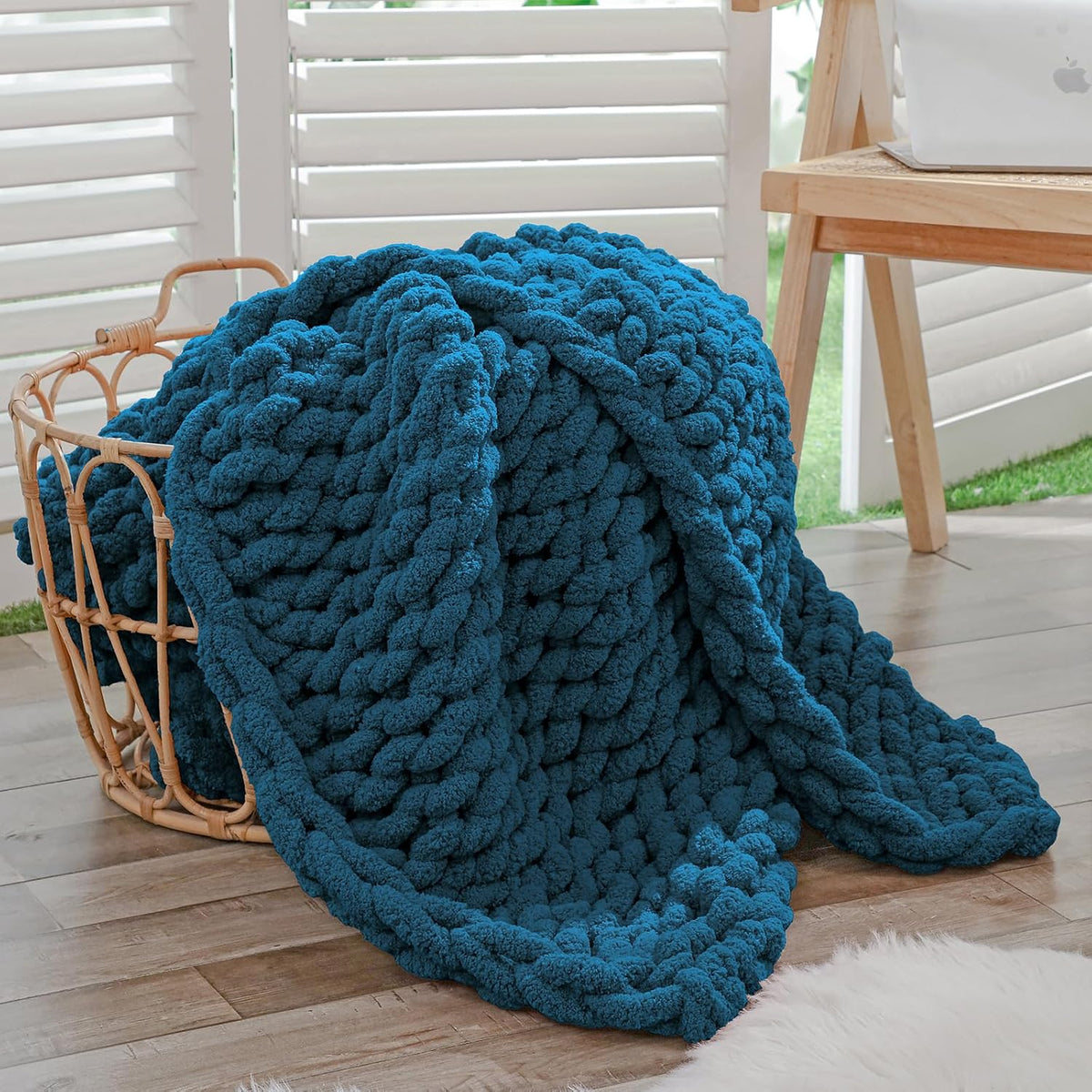 Deep teal chunky knit throw casually piled inside a woven basket beside a wooden desk.