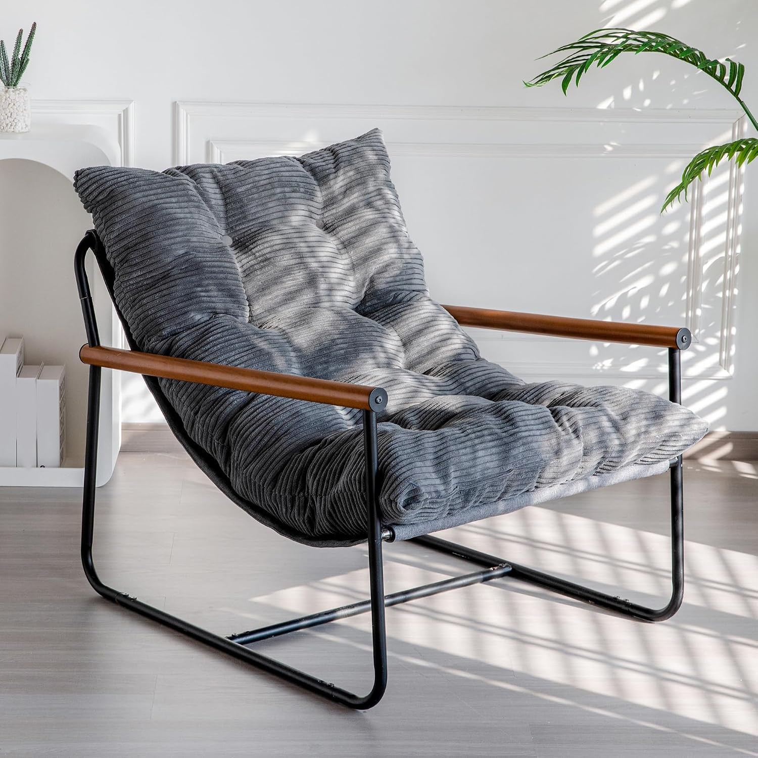 Low-profile corded fabric lounge chair with dark gray tufted cushion, black metal frame and wood armrests.