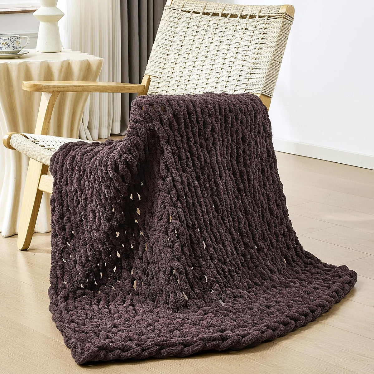Dark brown chunky knit throw casually draped over a woven-seat wooden chair.