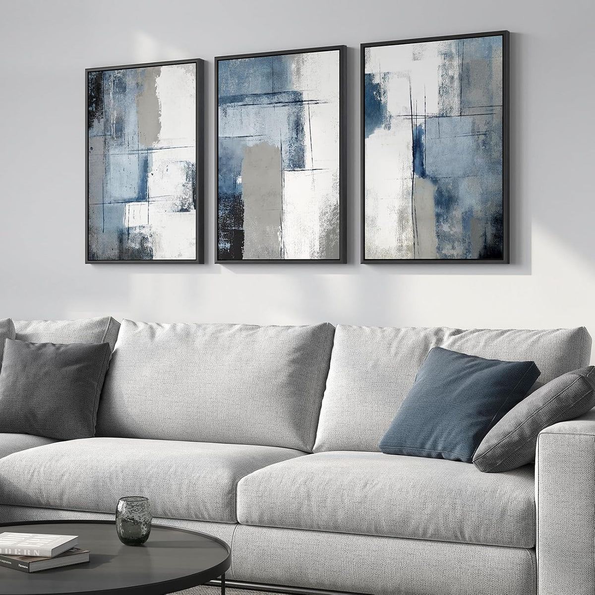 Close view of three framed blue-gray textured abstract panels hung above a light gray couch.