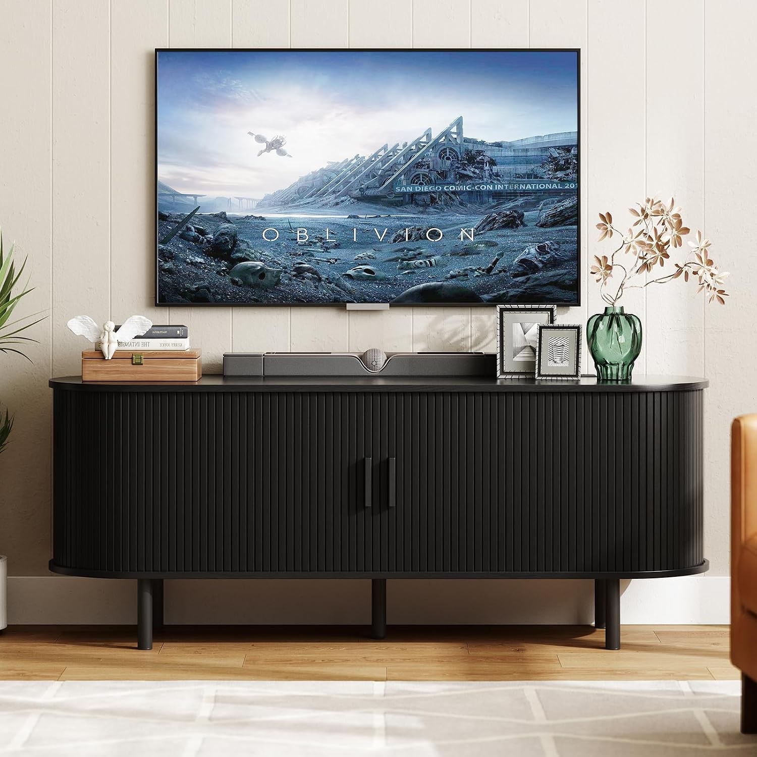 Closer front view of the black TV stand showing central handles, soundbar and decorative objects on top.