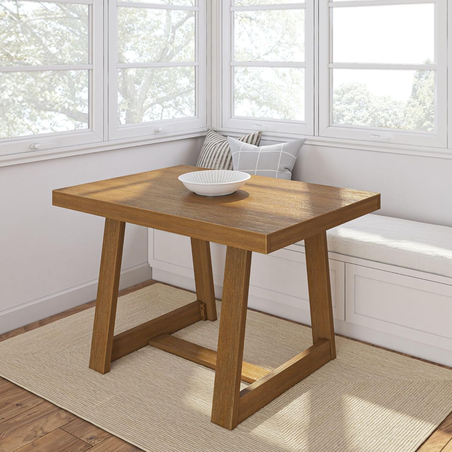 Square dining table with trestle-style legs in a warm pecan wood finish in a sunny nook