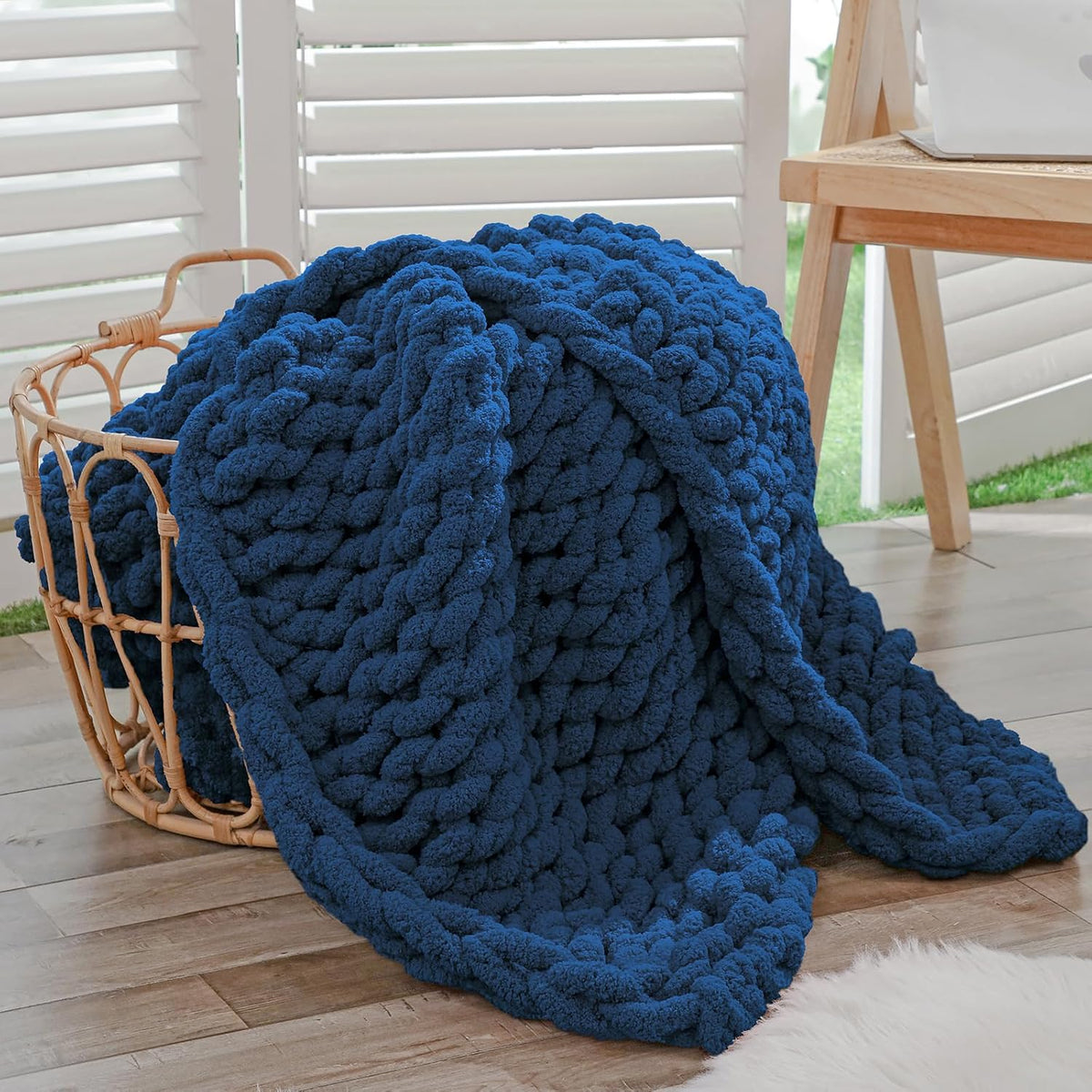 Deep blue chunky knit blanket overflowing from a woven basket on a wood floor.