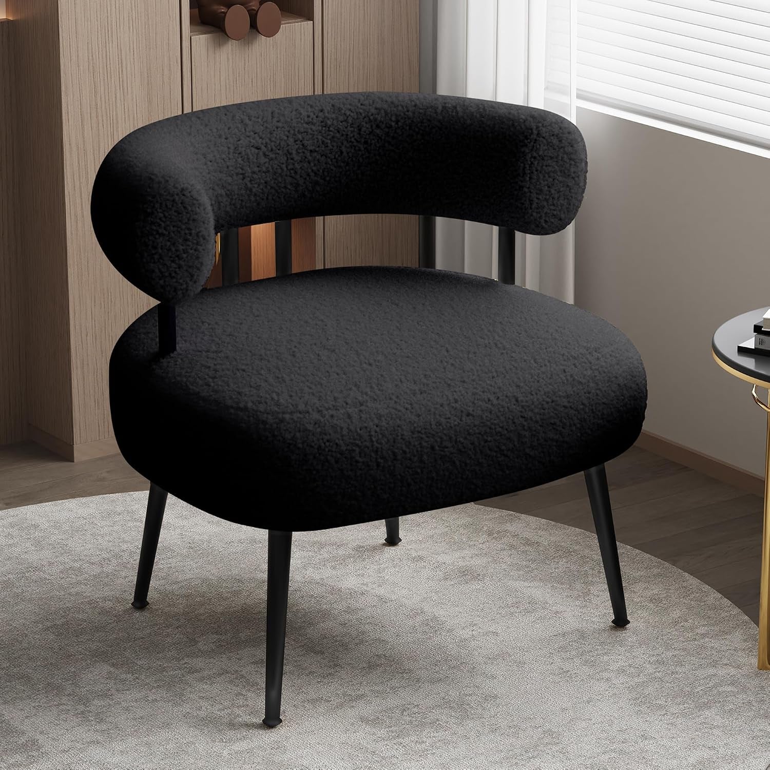 Black sherpa barrel chair with slim black legs placed on a light gray round rug near a window.