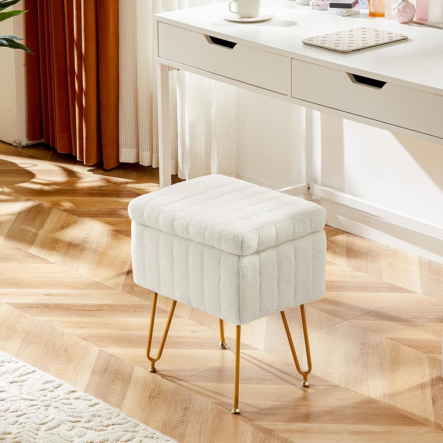 White faux-fur vanity stool with gold legs placed in front of a white desk on wood floors