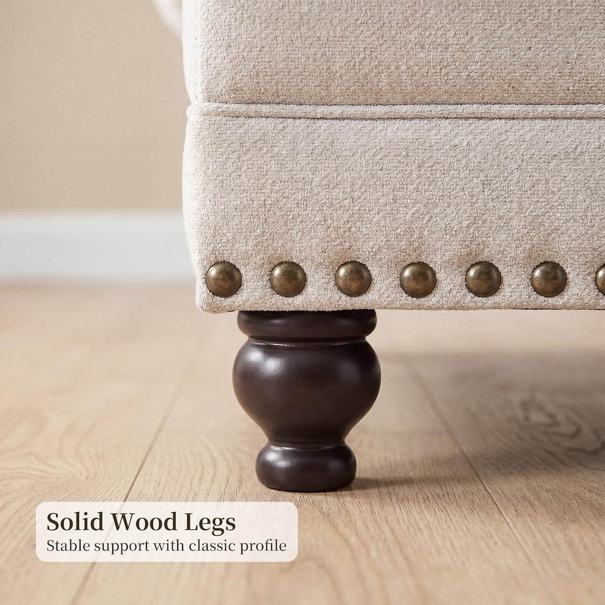 Turned dark wood leg and row of antique brass nailheads along the sofa base in close detail