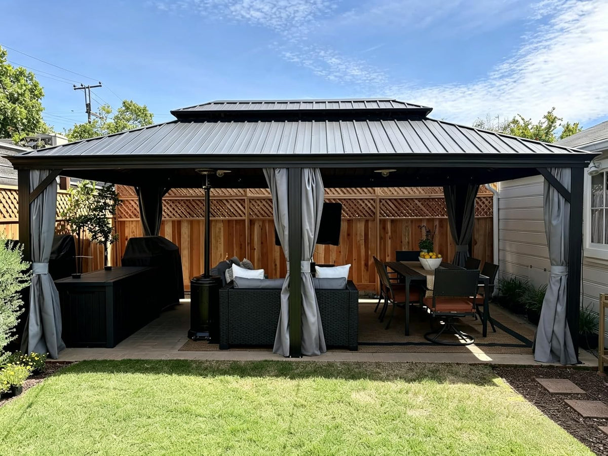 Front view of a gray metal gazebo with tied gray curtains over a patio seating and dining area, lawn in foreground.