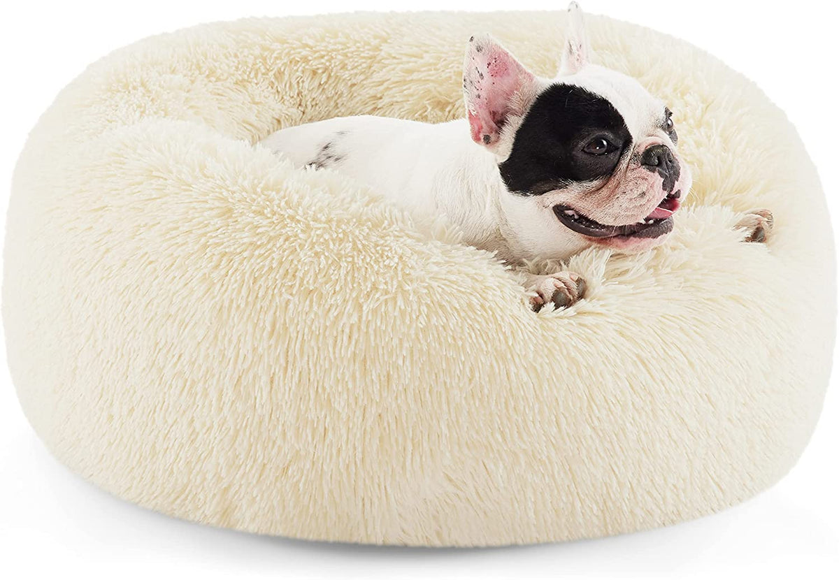 Three-quarter view of a cream-colored faux-fur donut dog bed with a black-and-white French bulldog lounging inside.