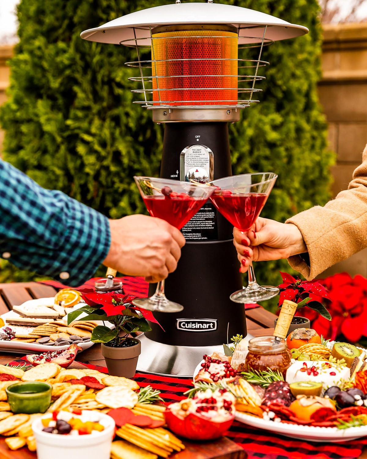 Outdoor party scene with the heater on a table as two people clink cocktail glasses over a spread of food.