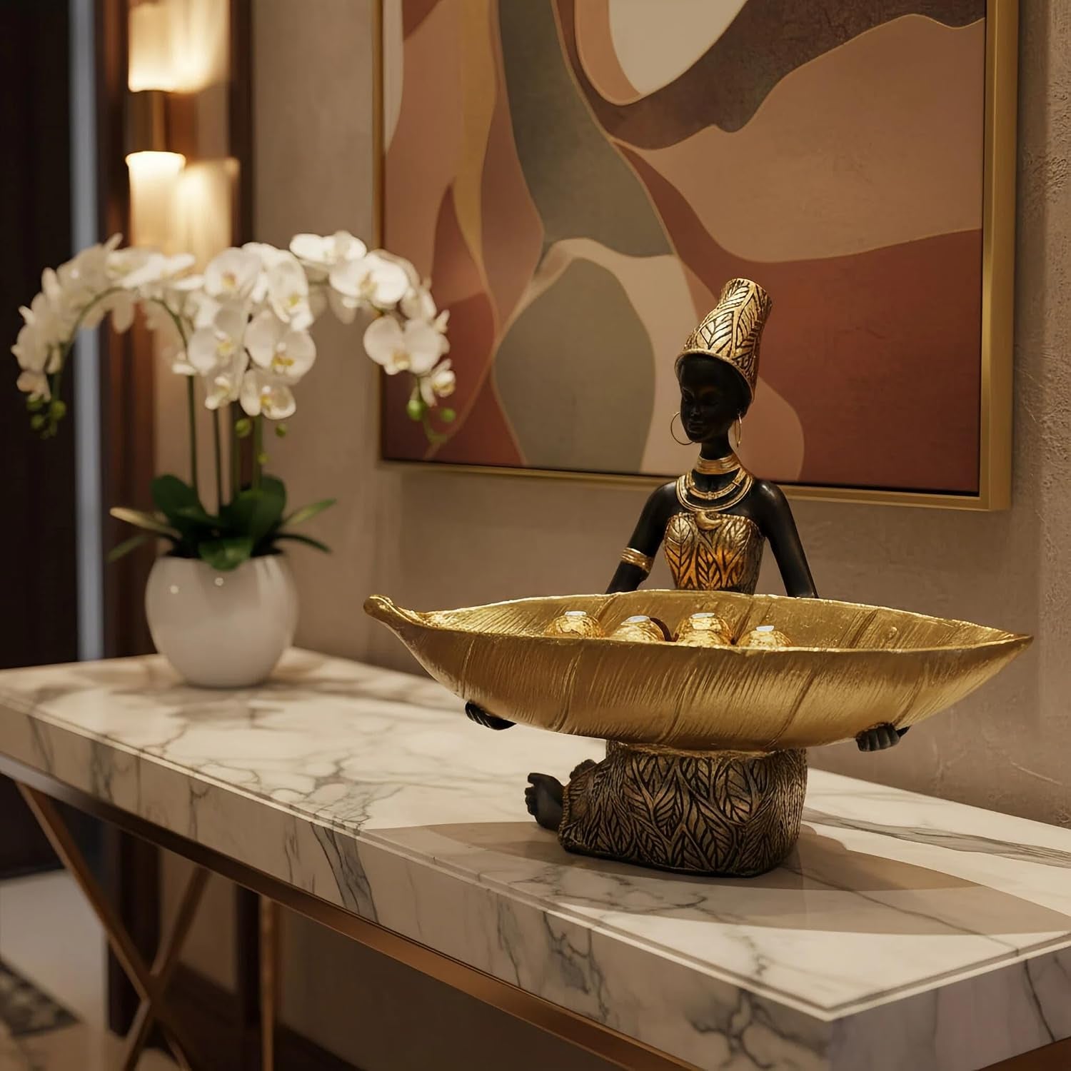 Black resin figurine with a gilded leaf tray displayed on a marble console table with orchids and framed wall art