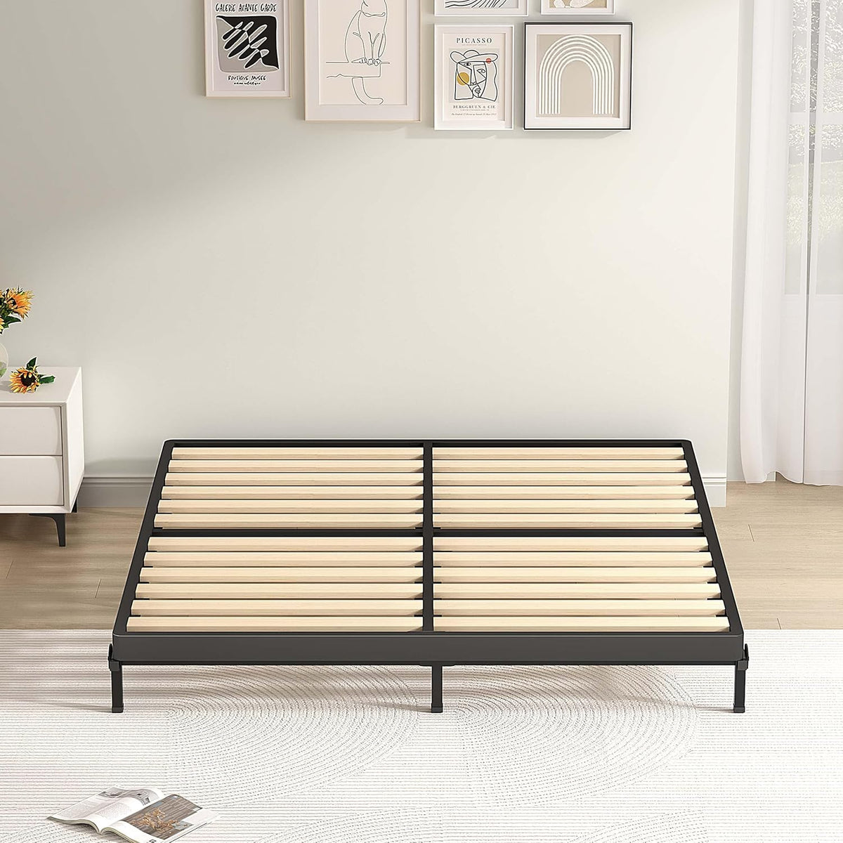 Low black metal bed frame with wooden slats set on a white rug in a bright bedroom.