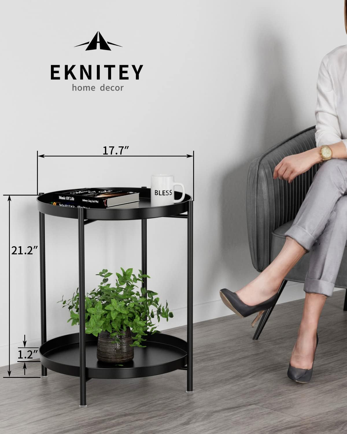 Black two-tier round side table shown with dimension arrows and a plant and mug on top, person seated nearby.
