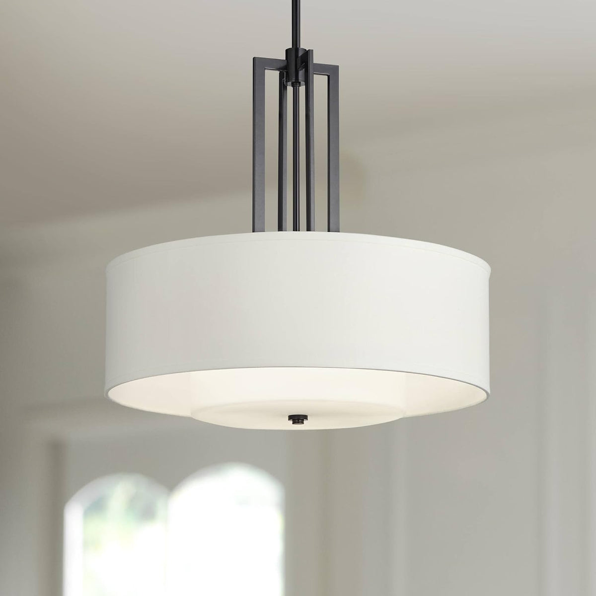 Installed drum pendant with black vertical support bars and white double-layer shade, shown in a bright interior.