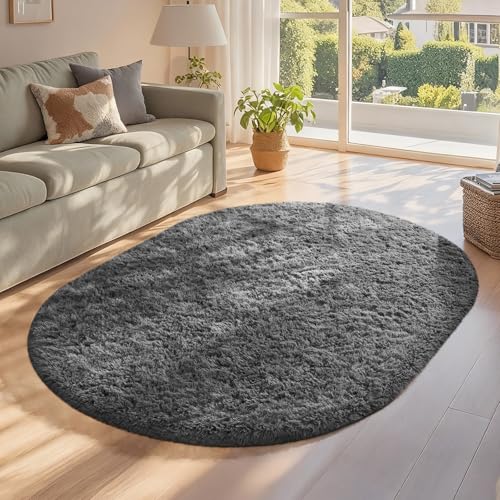 Oval dark gray shag area rug on light wood floor in a sunlit living room by a sofa and large window