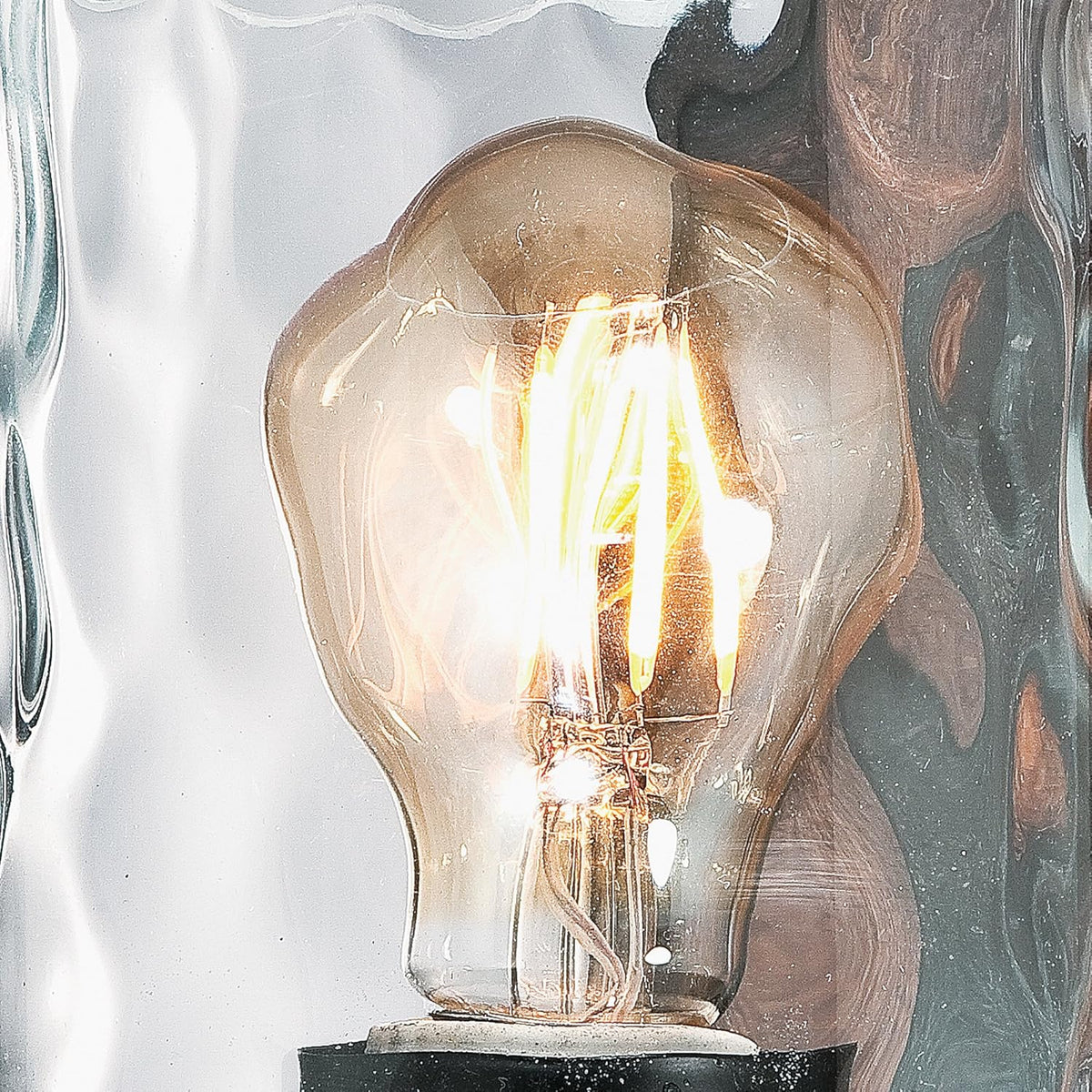 Tight view of lit filament-style bulb inside clear hammered glass shade with wood-tone back plate behind