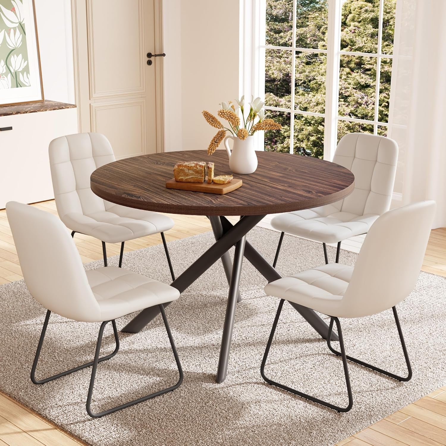 Round dark-walnut dining table with crossed metal legs surrounded by four white padded sled-base chairs.
