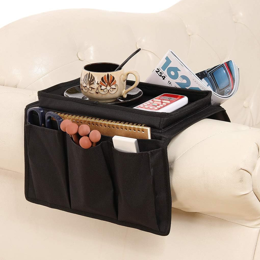 Black armrest caddy draped over a cream sofa arm holding a cup, remote and magazines