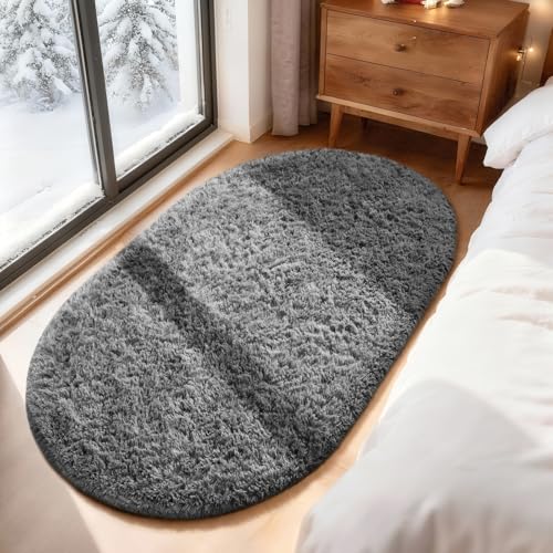 Oval gray shag rug placed beside a bed near a window and wooden nightstand with snow visible outside.