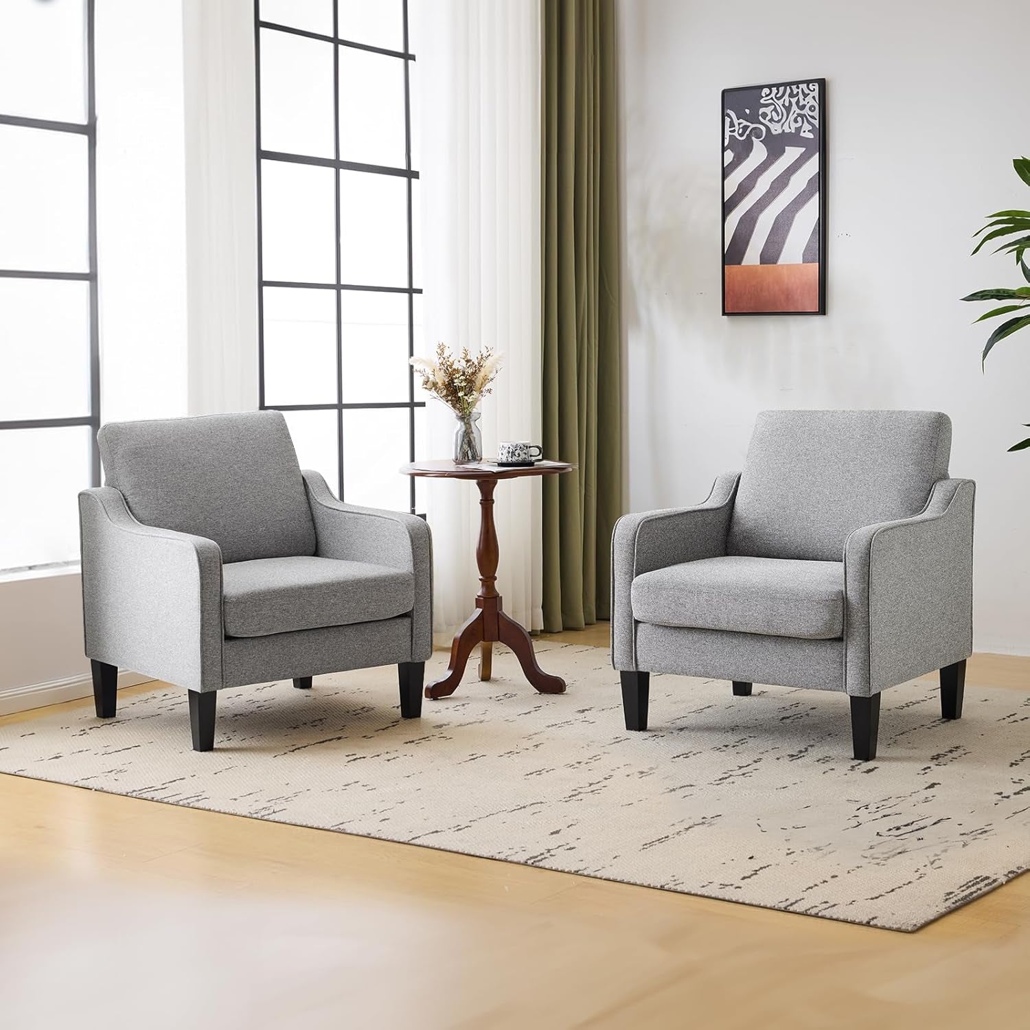 Pair of light gray upholstered accent chairs flanking a small round table in a sunny room.