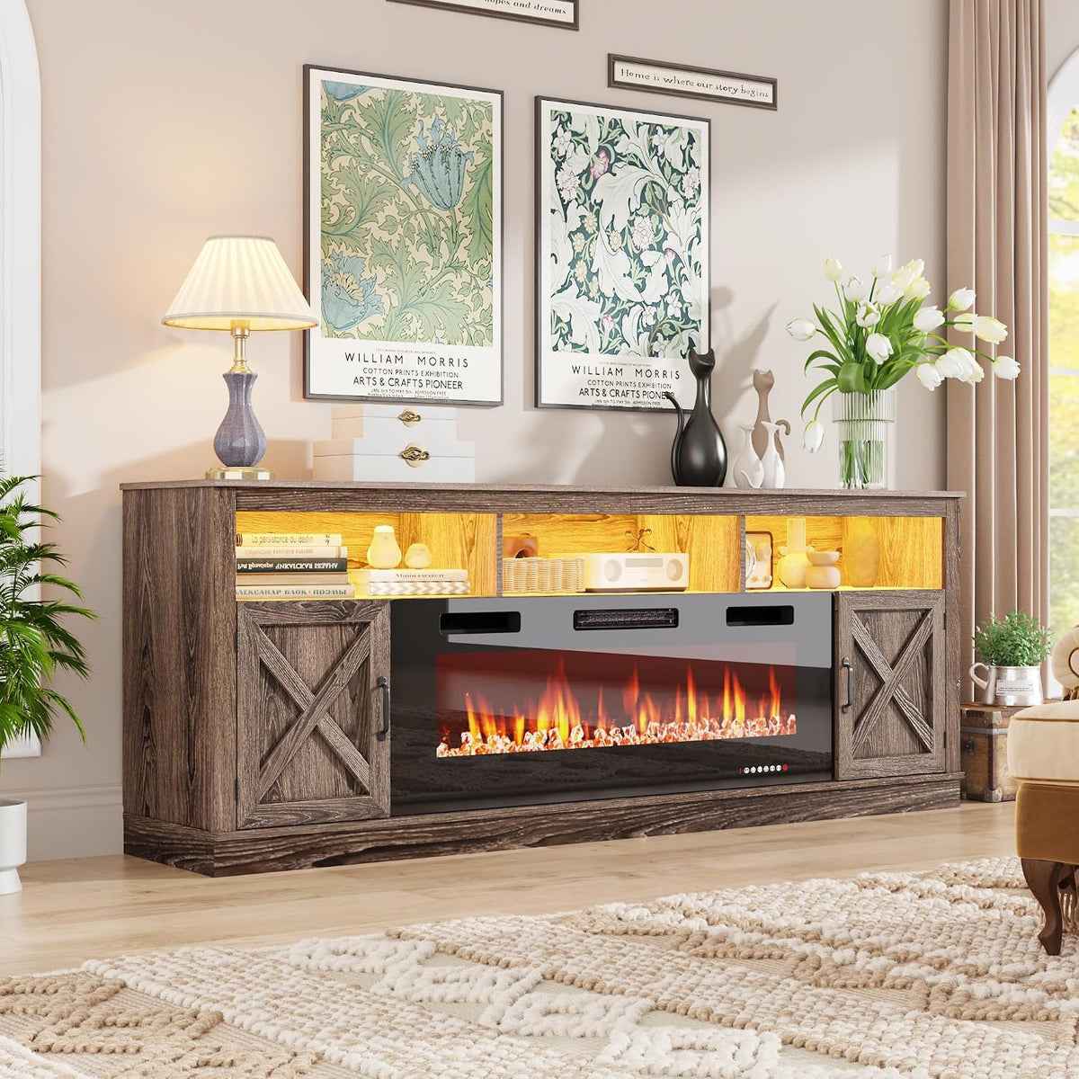 Brown farmhouse console with lit electric fireplace, table lamp on left and white tulips in a vase on right.