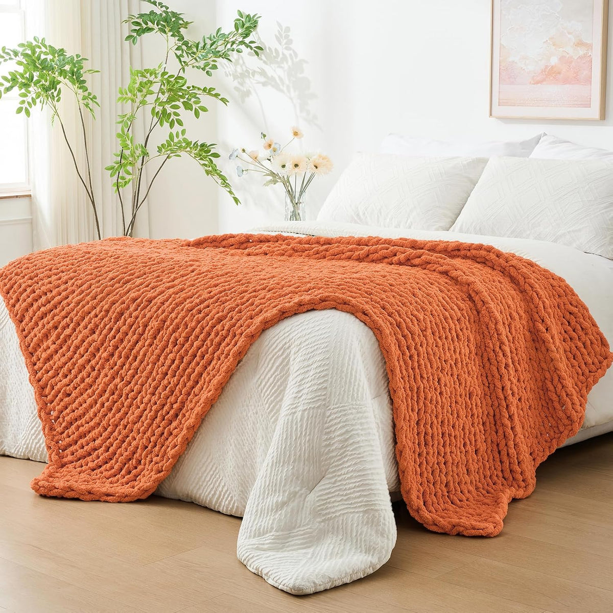 Orange chunky knit throw draped across the foot of a white bed in a bright bedroom