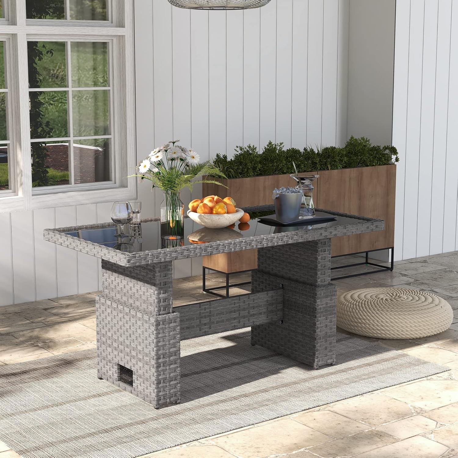 Grey resin wicker lift-top rectangular table with glass top, angled outdoor patio view with planter and round pouf
