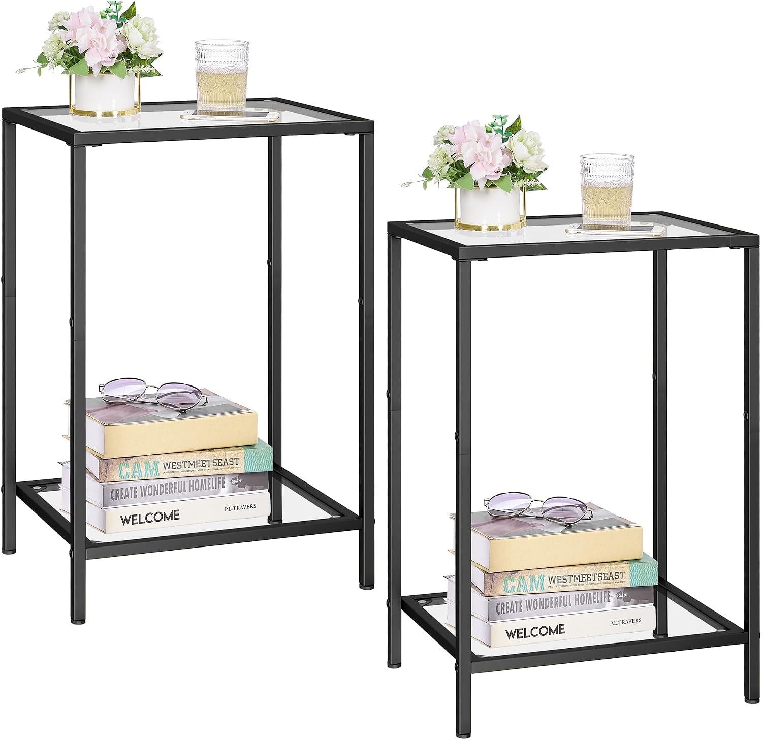 Two black metal-framed side tables with clear glass top and lower shelf, styled with books, flowers and a glass.