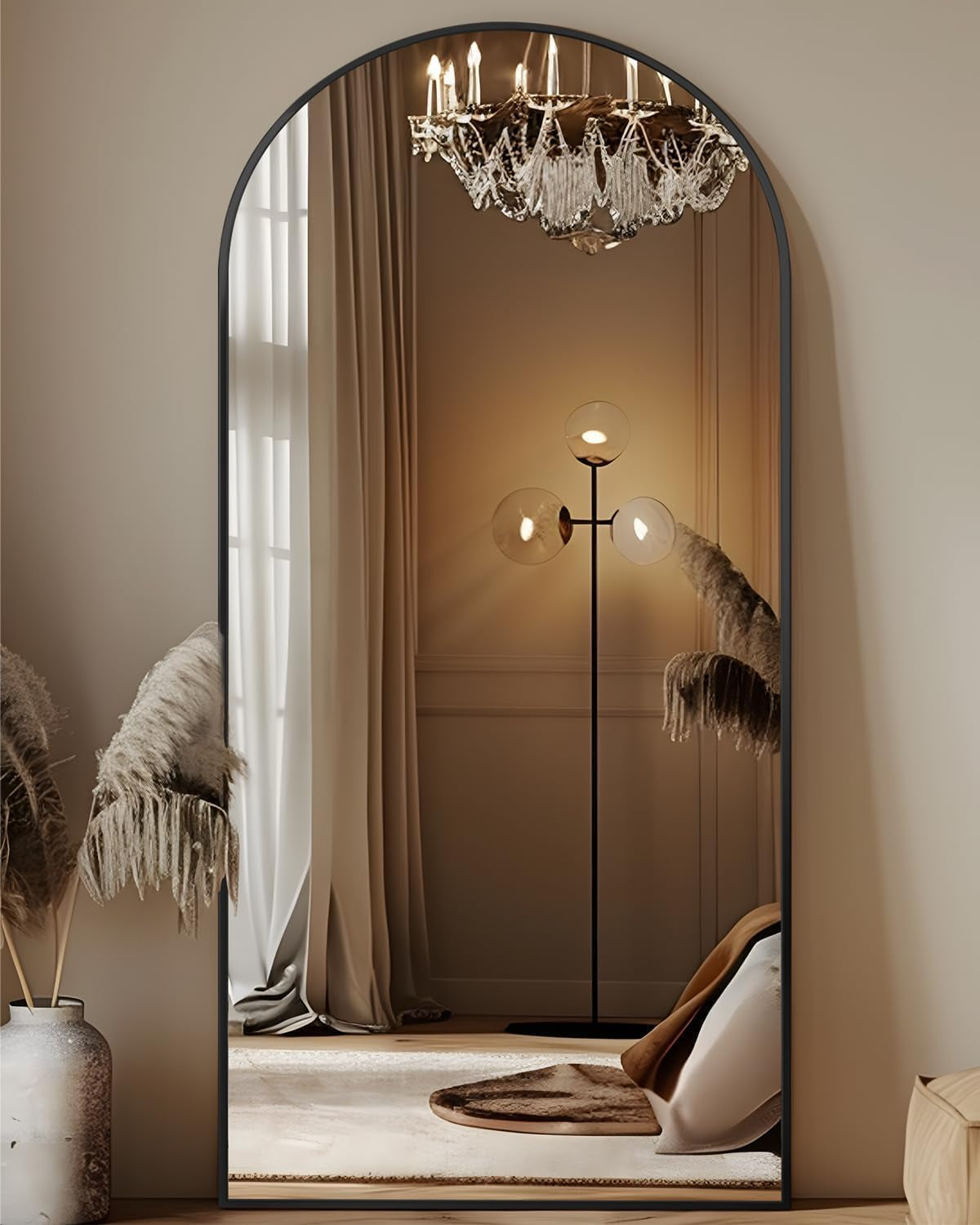 Arched full-length mirror with a slim black frame reflecting a chandelier and floor lamp.