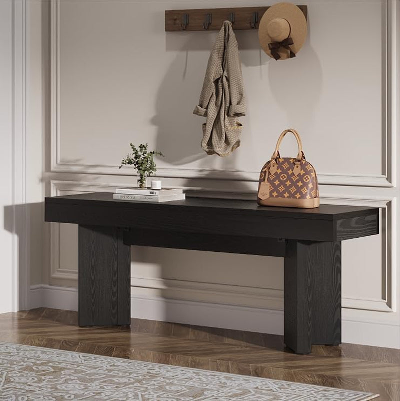 Black-finished bench in an entryway beneath wall hooks with a small handbag on top and a woven rug below.