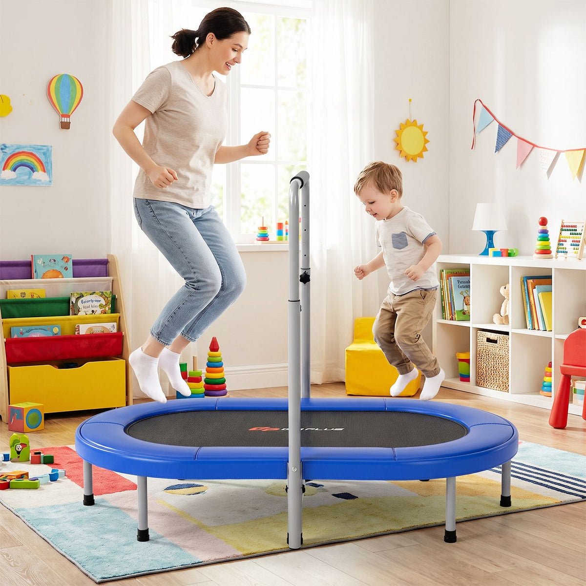 A woman and child bounce together on a blue trampoline with a tall support handle.