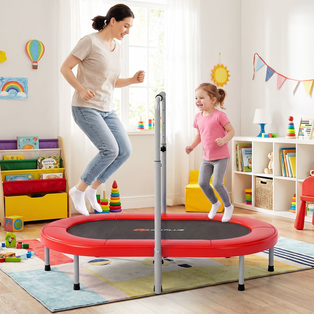 An adult and a child bounce on a red trampoline in a colorful playroom.