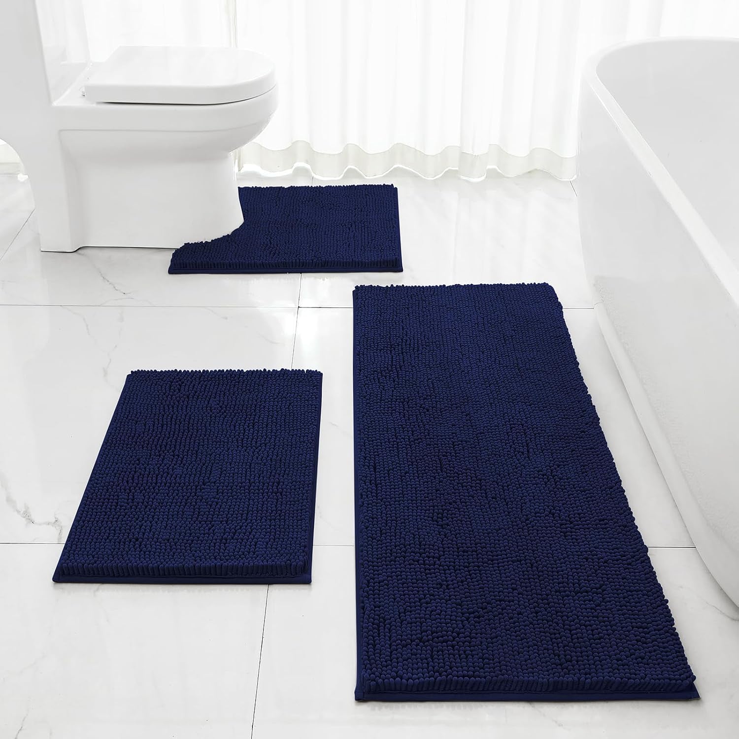 Dark navy chenille bath rug set placed on a white tiled bathroom floor beside a toilet and bathtub
