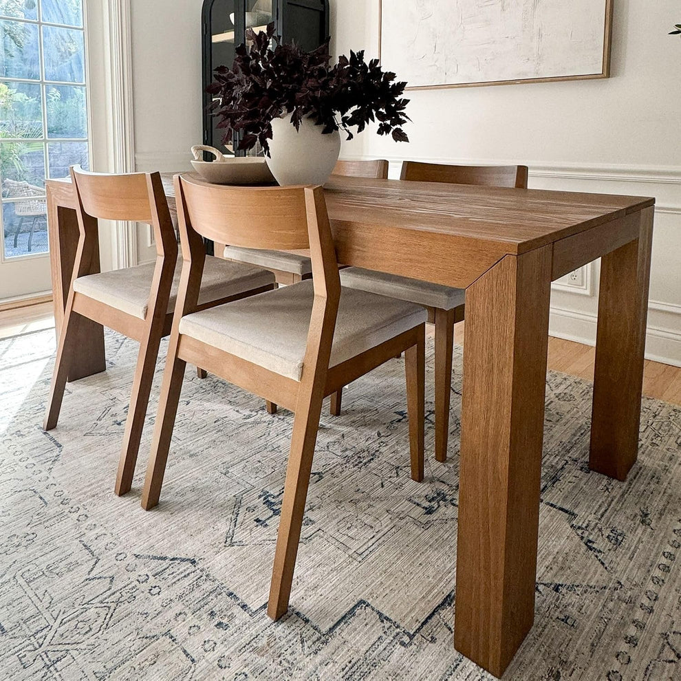 Angled dining room view of a solid pine table with four matching chairs on a patterned rug.