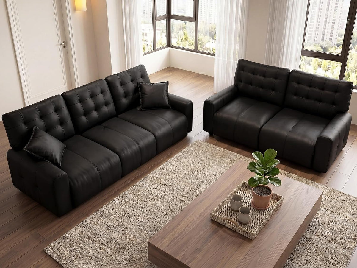 Two black tufted leather sofas (longer three-seat left, two-seat right) in a sunlit living room with coffee table and rug.