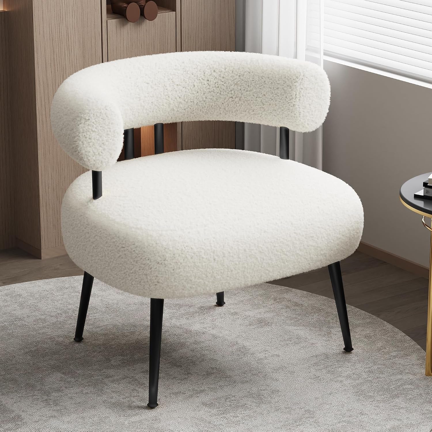Ivory sherpa barrel chair with black slender legs placed on a round rug beside a window and side table.