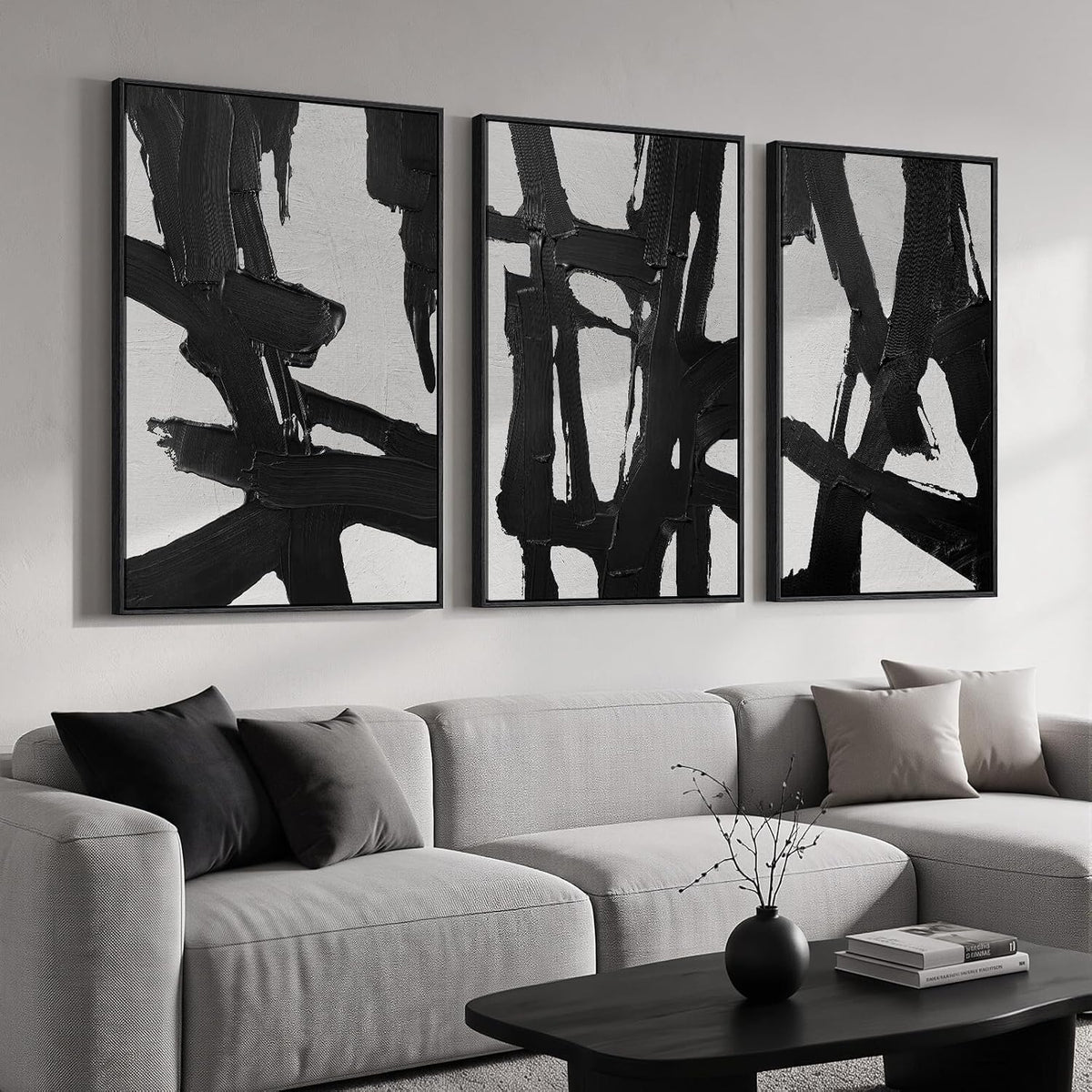 Three vertical canvases with bold black brushstrokes in slim black frames above a pale sectional and black coffee table.
