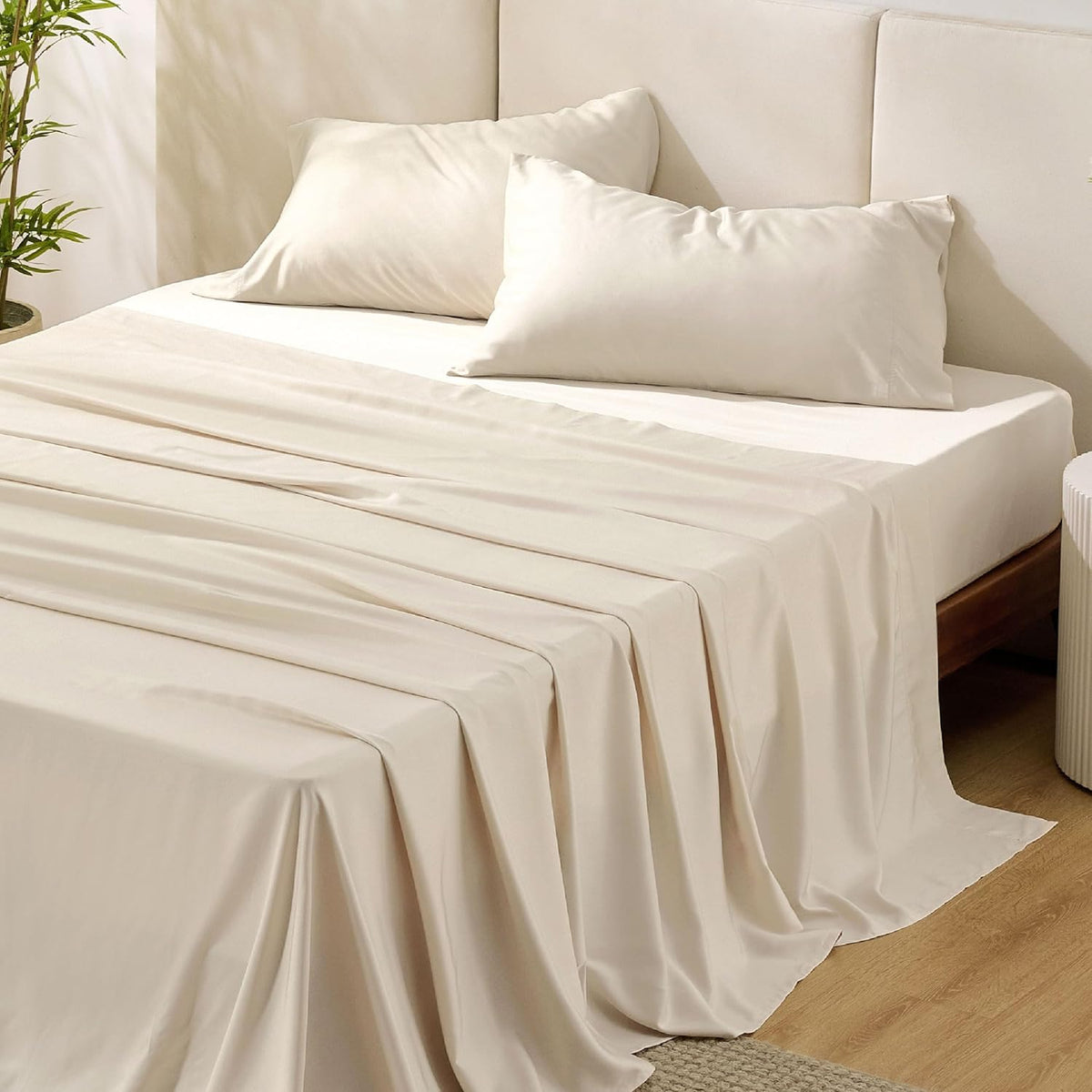 Cream/ivory sheets with two pillows on a bed with a padded headboard and a textured rug at the foot.