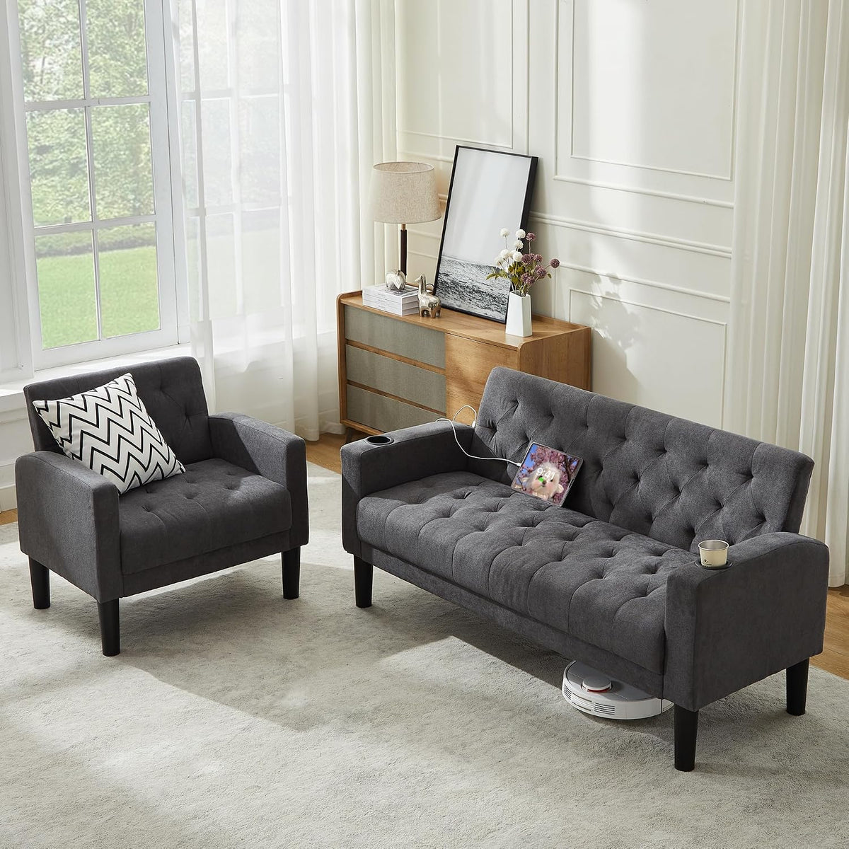 Bright room shot of the gray loveseat and matching armchair with tufted cushions and a tablet charging on the sofa.